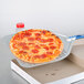 A pizza on a square perforated pizza peel with a long handle.
