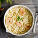 A white Bon Chef porcelain pasta bowl filled with pasta, shrimp, and a green leaf.