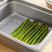 A Choice stainless steel pan grate with asparagus in it on a table.