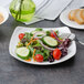 A salad with cucumber, tomatoes, and lettuce on a Bon Chef white porcelain salad plate.