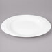 A white Bon Chef porcelain oval dinner plate with a rim on a gray surface.