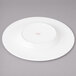 A white Bon Chef porcelain dinner plate with a red concentric circle design on a gray surface.