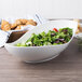 A white porcelain canoe bowl filled with salad next to a basket of croissants.