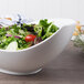 A 10 Strawberry Street Whittier white porcelain canoe bowl filled with salad on a table.
