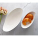 Two 10 Strawberry Street white porcelain canoe bowls filled with croissants on a white oval plate next to a bouquet of flowers.