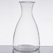 A clear glass decanter with a circular rim on a table.