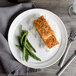 A Bon Chef white porcelain plate with salmon, rice, and green beans on a table.