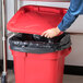 A person opening a red Rubbermaid BRUTE trash can with a black snap-lock lid.