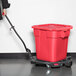 A woman pushing a red Rubbermaid BRUTE trash can with a black handle.