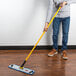 A man using a Rubbermaid HYGEN microfiber mop with a yellow handle to clean a hardwood floor.