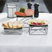A table with a Tablecraft chrome metal riser set holding plates of bread, grapes, and butter.