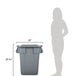 A woman standing next to a Rubbermaid grey square trash can with a lid.