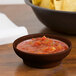 A brown GET salsa dish filled with salsa next to a bowl of chips.