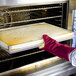 A person in a San Jamar Cool Touch Flame oven mitt putting a tray of food into an oven.
