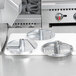 A Robot Coupe stainless steel food processor with three circular metal blades on a counter.