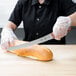 A person using a Mercer Culinary Praxis bread knife to cut a loaf of bread on a counter.