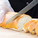 A person using a Mercer Praxis curved bread knife to cut a loaf of bread.