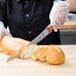 A person using a Mercer Praxis curved bread knife to slice bread.