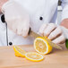 A person in white gloves using a Mercer Culinary Millennia utility knife to slice a lemon.