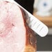 A Mercer Culinary Praxis slicer knife with a rosewood handle cutting a piece of ham.