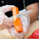 A person in gloves using a Mercer Culinary Praxis paring knife to peel a carrot.