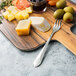 A cutting board with cheese, olives, and a Walco stainless steel cocktail fork.
