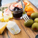 A Walco stainless steel cocktail fork spearing cheese and olives on a wooden board.