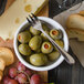 A Walco stainless steel cocktail fork in a bowl of olives and grapes.