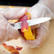A person peeling a peach with a Mercer Culinary Praxis paring knife.