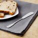 A Walco stainless steel butter spreader on a napkin next to a plate of bread.