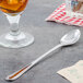 A Walco stainless steel iced tea spoon next to a glass of tea on a table.