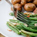 A Walco stainless steel table fork spearing green beans and potatoes on a plate.