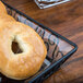 A bagel in an American Metalcraft clear PET basket liner on a table in a bakery display.