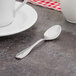 A Walco Saville demitasse spoon on a table next to a white cup.