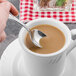 A finger holding a Walco stainless steel demitasse spoon over a cup of coffee.