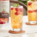 A glass of Monin raspberry lemonade with ice, lemons, and raspberries on a coaster.