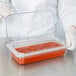 A person in white gloves using a Carlisle clear plastic container with red sauce.