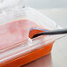 A Carlisle clear polycarbonate hinged lid with a spoon in a plastic container of sauce.