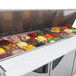 A Turbo Air 3 door refrigerated sandwich prep table with food trays holding different types of food on a counter.
