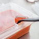 A Carlisle clear polycarbonate hinged lid with two notches on a container of food with a plastic spoon.