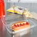 A hot dog with ketchup in a Dart clear hinged plastic container on a counter.