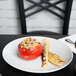 A Tuxton bright white oval china platter with a tomato stuffed with rice and a piece of grilled corn on the table.