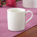 A Villeroy & Boch white bone porcelain cup with a white handle on a pink table