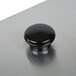 A black round cover with a black knob on a metal surface.