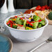 A white melamine bowl filled with salad and vegetables with a fork.