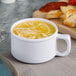 A white Thunder Group melamine soup mug with soup in it next to a plate of bread.