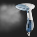 A white Conair handheld steamer with steam coming out of it.