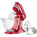 A red KitchenAid stand mixer with a glass bowl and whisk.