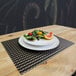 A plate of salad on a black woven vinyl rectangle placemat.