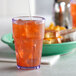 A close up of a GET Bahama blue plastic tumbler filled with orange liquid and ice with a straw.